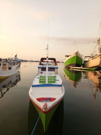 Fishing boats moored on sea during sunset