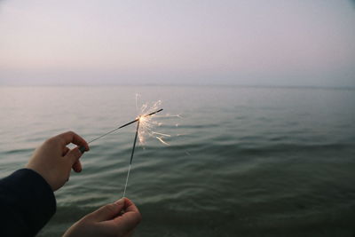 Close-up of hand holding sea against sky during sunset