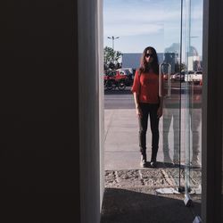 Full length of woman standing by glass door in city