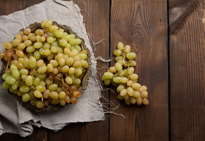 Green grapes in a wooden round plate on a black table, top view