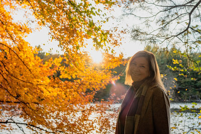 Portrait of woman standing by tree during autumn