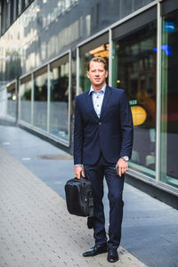 Portrait of mature businessman with bag standing against office building