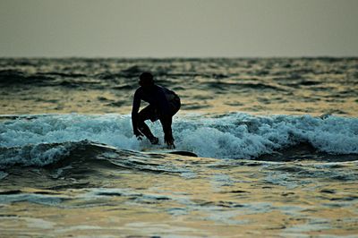 Silhouette man surfing in sea at sunset