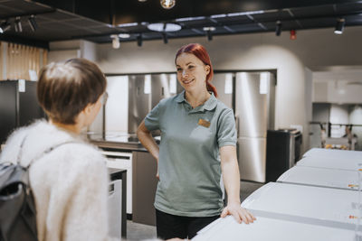 Smiling saleswoman advising female customer in buying appliance at electronics store