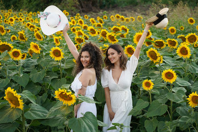 Portrait of female friends standing amidst sunflowers