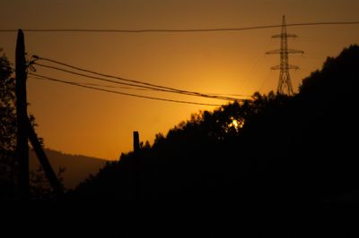 Low angle view of silhouette electricity pylon against sky during sunset