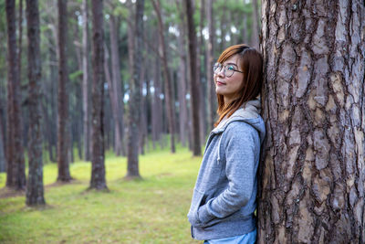 Side view of woman standing by tree trunk in forest