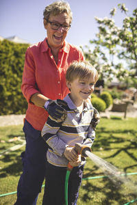 Happy grandmother and grandson spraying water in yard