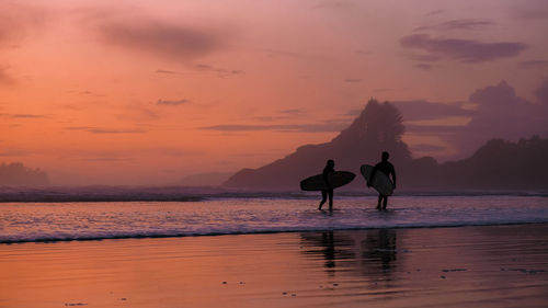 Silhouette people at beach against sky during sunset