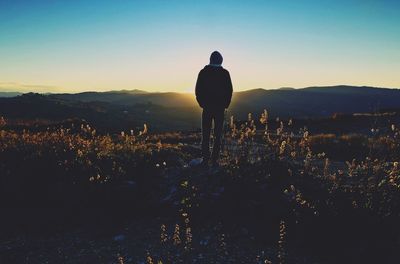 Rear view of silhouette man standing on landscape against sky