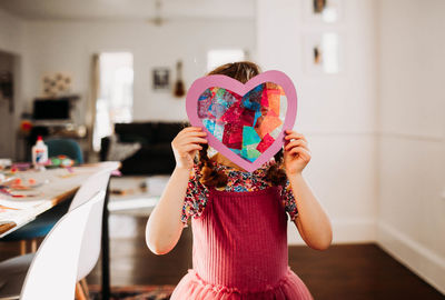 Young girl standing inside with rainbow heart in hands