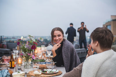 Smiling female friends talking while sitting on terrace during social gathering
