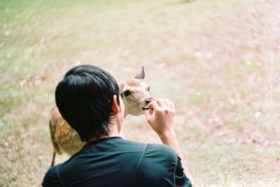 Rear view of teenage boy feeding deer