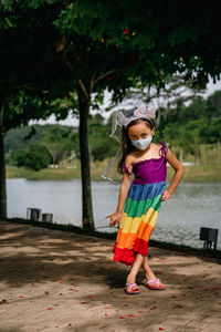 Little girl wearing face mask with rainbow dress enjoying outdoor in the park. new normal.