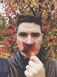 Portrait of man holding maple leaf against tree