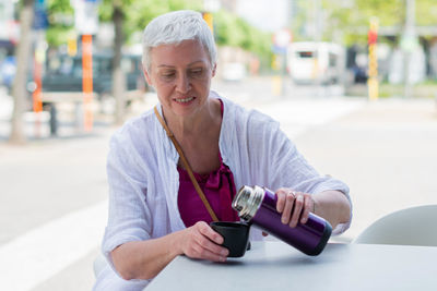 An aged woman with bob cut drink water from plastic bottle at the cafe table