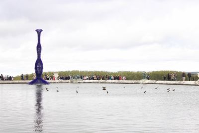 Group of people on riverbank against cloudy sky