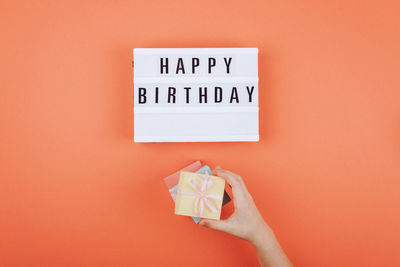Close-up of hand holding paper against orange background