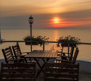 Chairs and tables on beach against sky during sunset