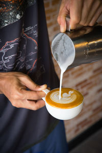 Midsection of man pouring milk in coffee