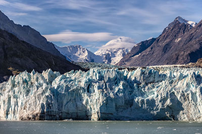 Snow covered landscape by sea against mountain range