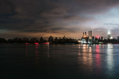 Illuminated buildings by river against sky during sunset