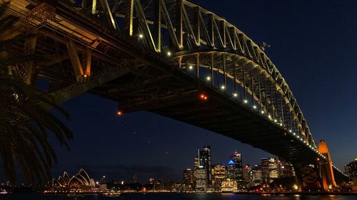 Low angle view of illuminated bridge and buildings against sky at night