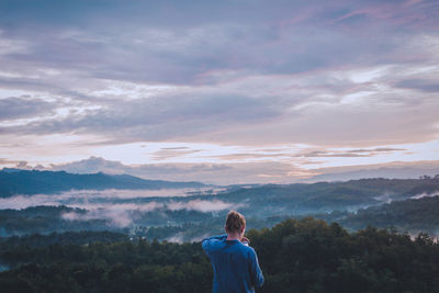 Rear view of man standing on mountain against sky