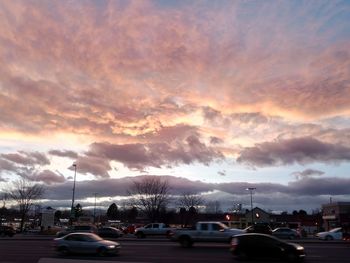 Cars on city street against dramatic sky