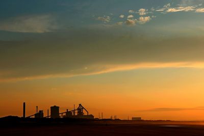 Silhouette of factory against sky during sunset