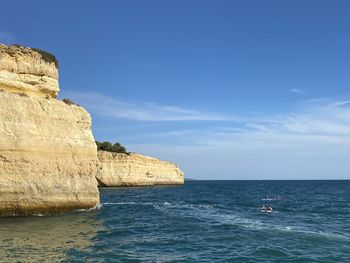 Rock formations by sea against blue sky