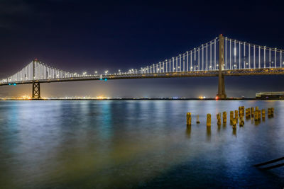 Illuminated bridge over river against sky at night