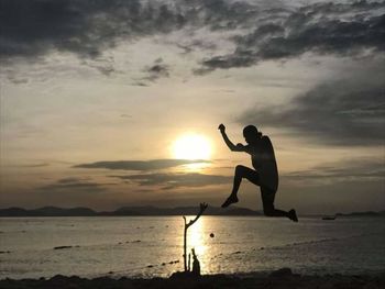 Silhouette men on shore against sky during sunset