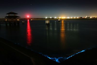 Illuminated city by sea against sky at night