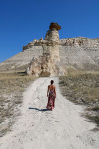 Rear view of woman standing on mountain against clear blue sky