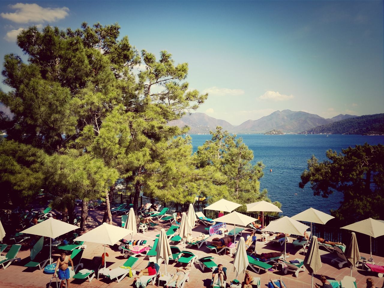 tree, water, mountain, sea, sky, beach, chair, relaxation, vacations, tranquil scene, nature, scenics, built structure, building exterior, tranquility, shore, table, day, beauty in nature