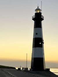 Lighthouse by sea against sky during sunset