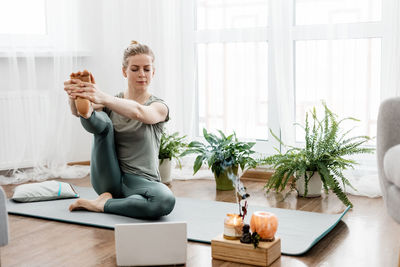 Athletic woman doing yoga and watching online lessons on laptop, exercising in living room