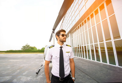 Portrait of young man standing on car against sky