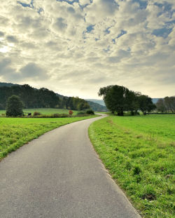 Footpath on grassy field against cloudy sky