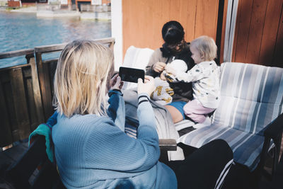 Friend photographing woman playing with children through smart phone at holiday villa