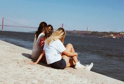 Rear view of women sitting on shore against sky