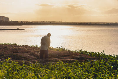 Rear view of man walking on field against sky during sunset