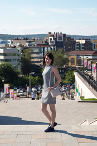 A brunette woman with a wide smile stands on a bridge against the background of the city sunny