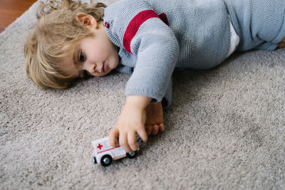 Cute little boy lying on carpet and playing with toy car in living room at home