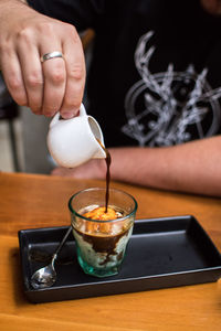 Close-up of hand pouring coffee in cup on table affogato
