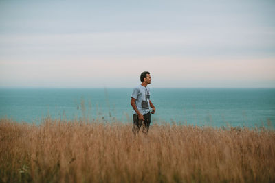 Man standing on cliff by sea against sky