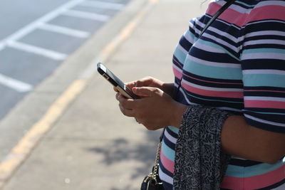 Midsection of woman using mobile phone while standing on sidewalk