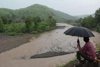 Man sitting on wet umbrella in rainy season