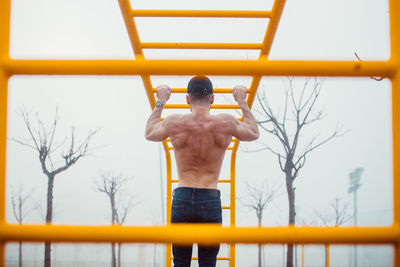 Man with cap doing pull-ups in a calisthenics park. back photo